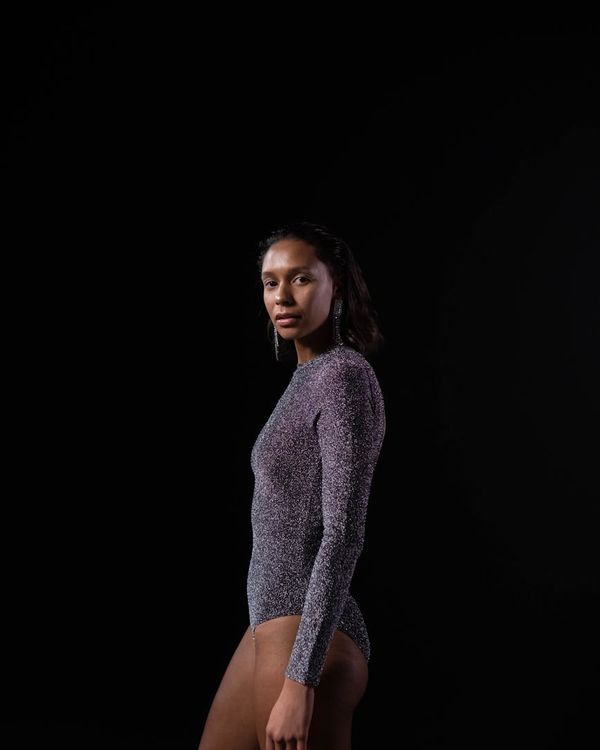 Woman in a calm yoga pose in a dark studio with coral light.